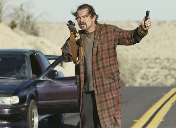 Man next to a car stopped on a road, holding a gun and some sort of device